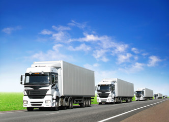 Fototapeta na wymiar karawana białych ciężarówek na autostradzie pod błękitnym niebem