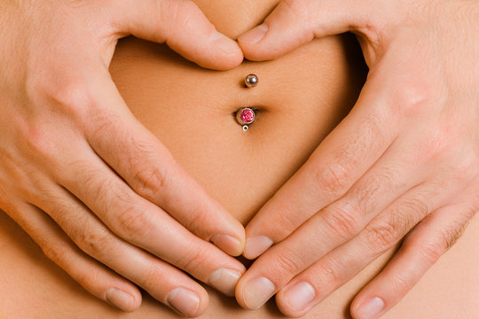 man's hands forming a heart symbol on woman's belly