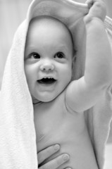 Child after bath in mothers hands under the soft towel smiling