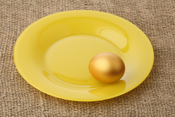 Gold egg on a plate against a sacking