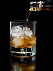 Pouring whisky with ice on black background