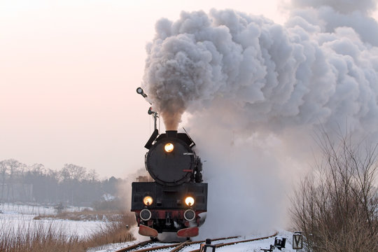 Fototapeta Retro steam train starting from the station during wintertime