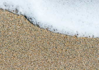 White sea foam beach background on a yellow brown sand grains