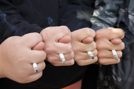 four hands of teens with fico gestures and cigarettes