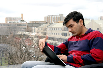 Young Indian student working on his laptop in the university. - obrazy, fototapety, plakaty
