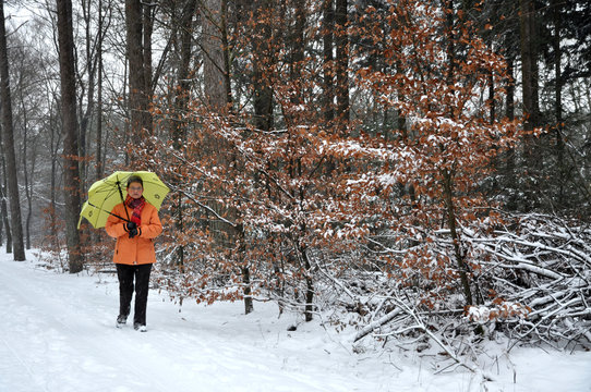 Senior woman walking in the snow with umbrella