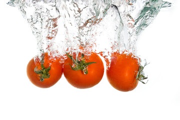 Three tomatos falling into clear water
