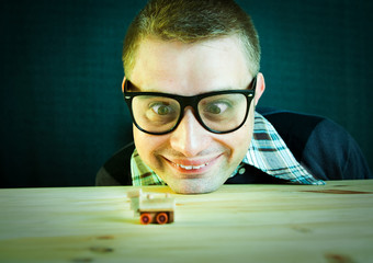 Funny nerd plays with small wooden train - focus on the face