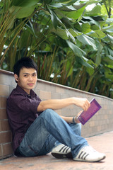 A young Asian man reading outdoors