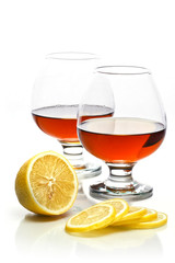 Two glasses of brandy with lemon on white background