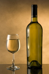 Bottle and glass of white wine with warm yellow background