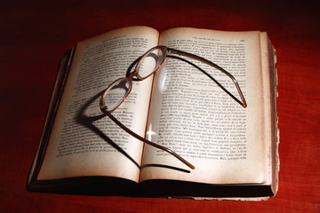 Old book and glasses on the desk.
