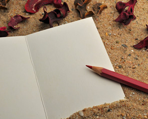 Karte im Sand mit rosa Bleistift und Rosenblättern