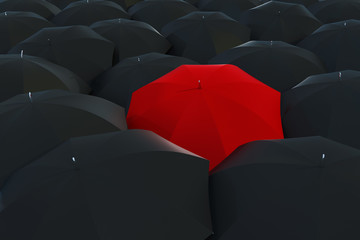 A single red umbrella surrounded by black umbrellas