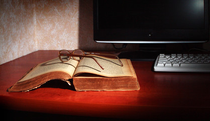 Old book, glasses, computer monitor and keyboard.
