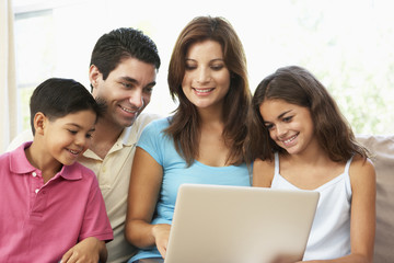 Family Sitting On Sofa At Home With Laptop