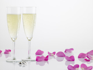 Two Wedding Rings Next To Champagne Flutes And Rose Petals