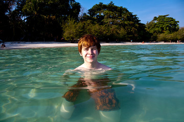 Junge kniet im Meer am klaren Traumstrand und geniesst