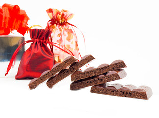 Some slices of black porous chocolate and gifts by a holiday
