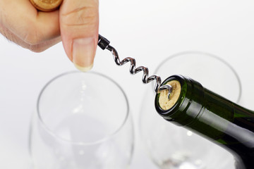 Opening a bottle of wine with wine glasses in the background © Adrin Shamsudin