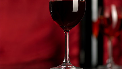The big glass of red wine and bottle on a red background