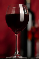 The big glass of red wine and bottle on a red background