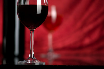 The big glass of red wine and bottle on a red background