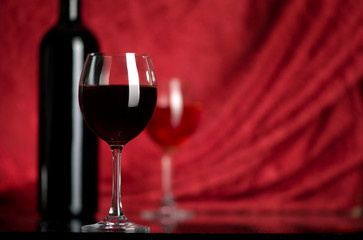 The big glass of red wine and bottle on a red background