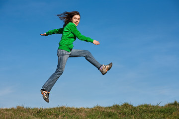 Girl running, jumping against blue sky