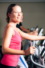 People exercising on elliptical trainer in gym