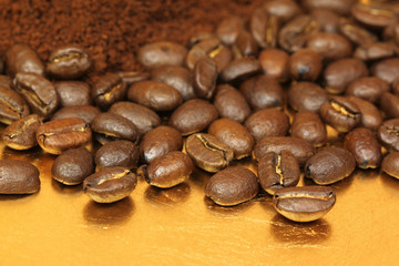 Whole roasted coffee arabic beans and ground on golden plate