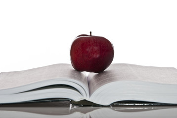 opened hefty book and fresh red apple