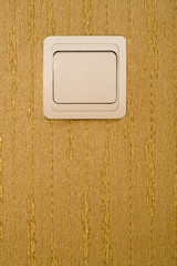 Light switch on a wall with wallpaper of gold color