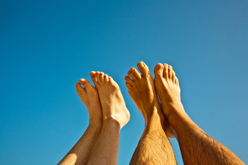 leg and feet of a man and a child in front of the clear blue sky
