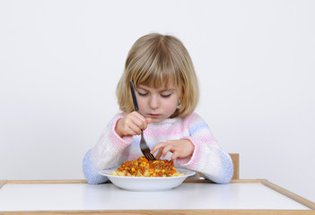 Kleines Maedchen stochert missmutig im Essen herum.