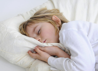 Kleines Maedchen liegt schlafend im Bett.
