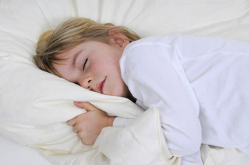 Kleines Maedchen liegt schlafend im Bett.