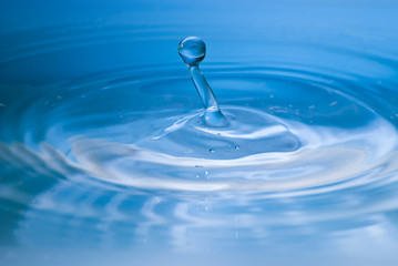 Fototapeta na wymiar Clean blue drop of water splashing in clear water. Abstract blue