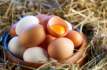 Chicken eggs in the straw with half a broken egg
