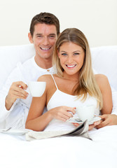 Obraz na płótnie Canvas Happy couple drinking coffee lying on their bed