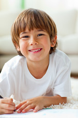 Happy little boy drawing lying on the floor