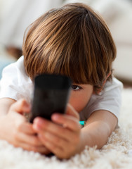 Adorable little boy holding a remote lying on the floor
