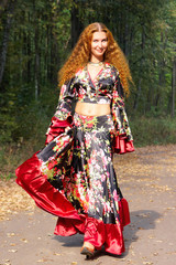 Beautiful ginger-haired girl in gypsy suit in forest