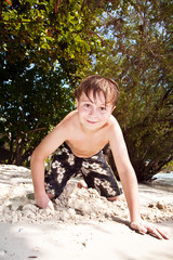 happy young boy is digging in the sand of the beach