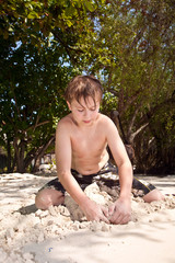 happy young boy is digging in the sand of the beach