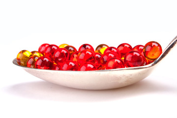 Spoon with red and yellow capsules isolated on white