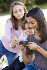 Teen girl texting on mobile phone while younger siblings watch