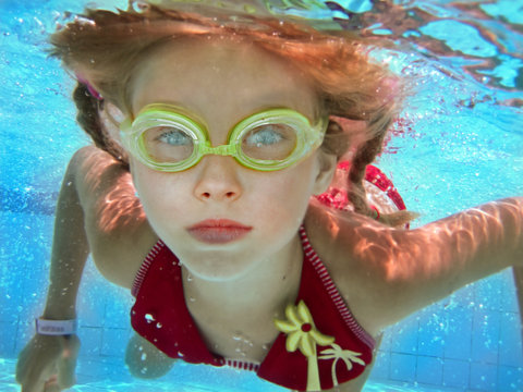 Child girl swim underwater in swimming pool.
