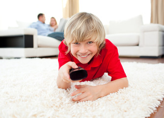 Happy boy holding a remote lying on the floor