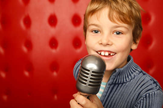Singing boy with microphone on rack against red wall
